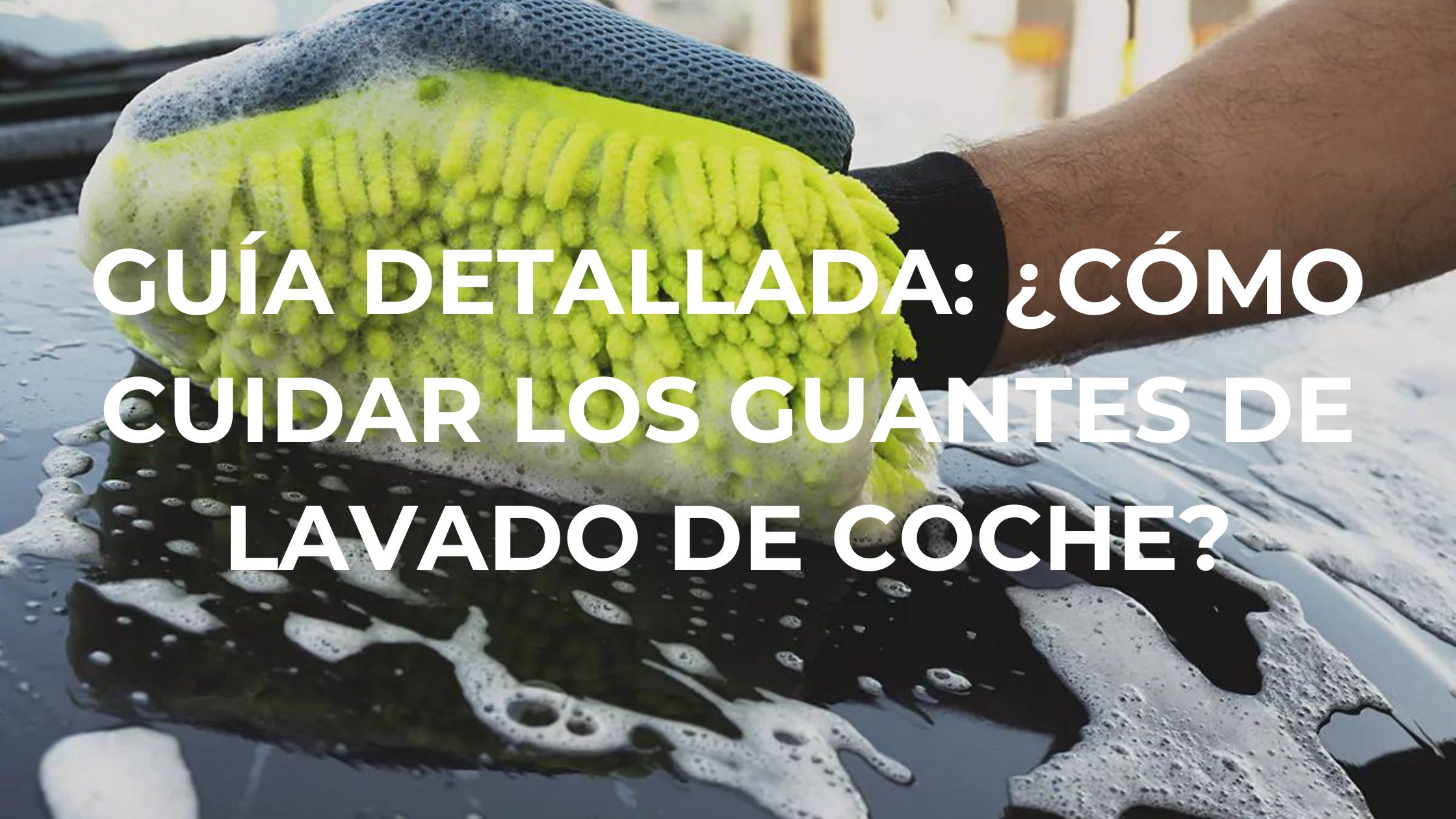 Una persona utilizando un guante de microfibra amarillo con espuma para lavar la superficie de un coche negro, lleno de jabón y agua.