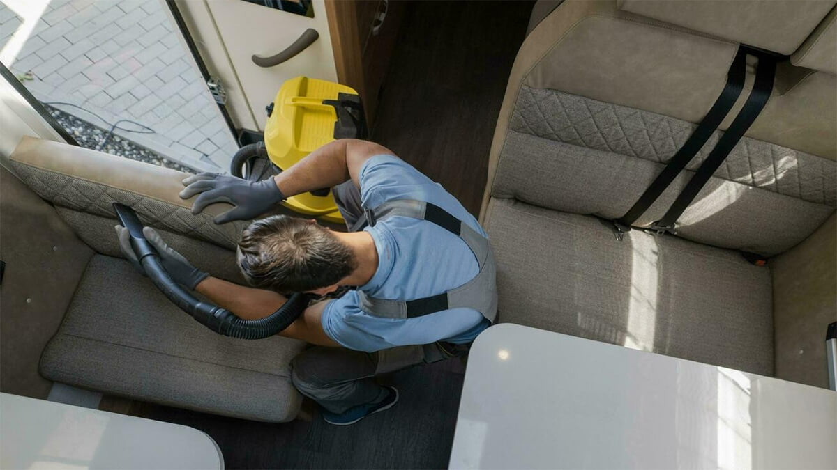Hombre aspirando la tapicería de un asiento de una autocaravana