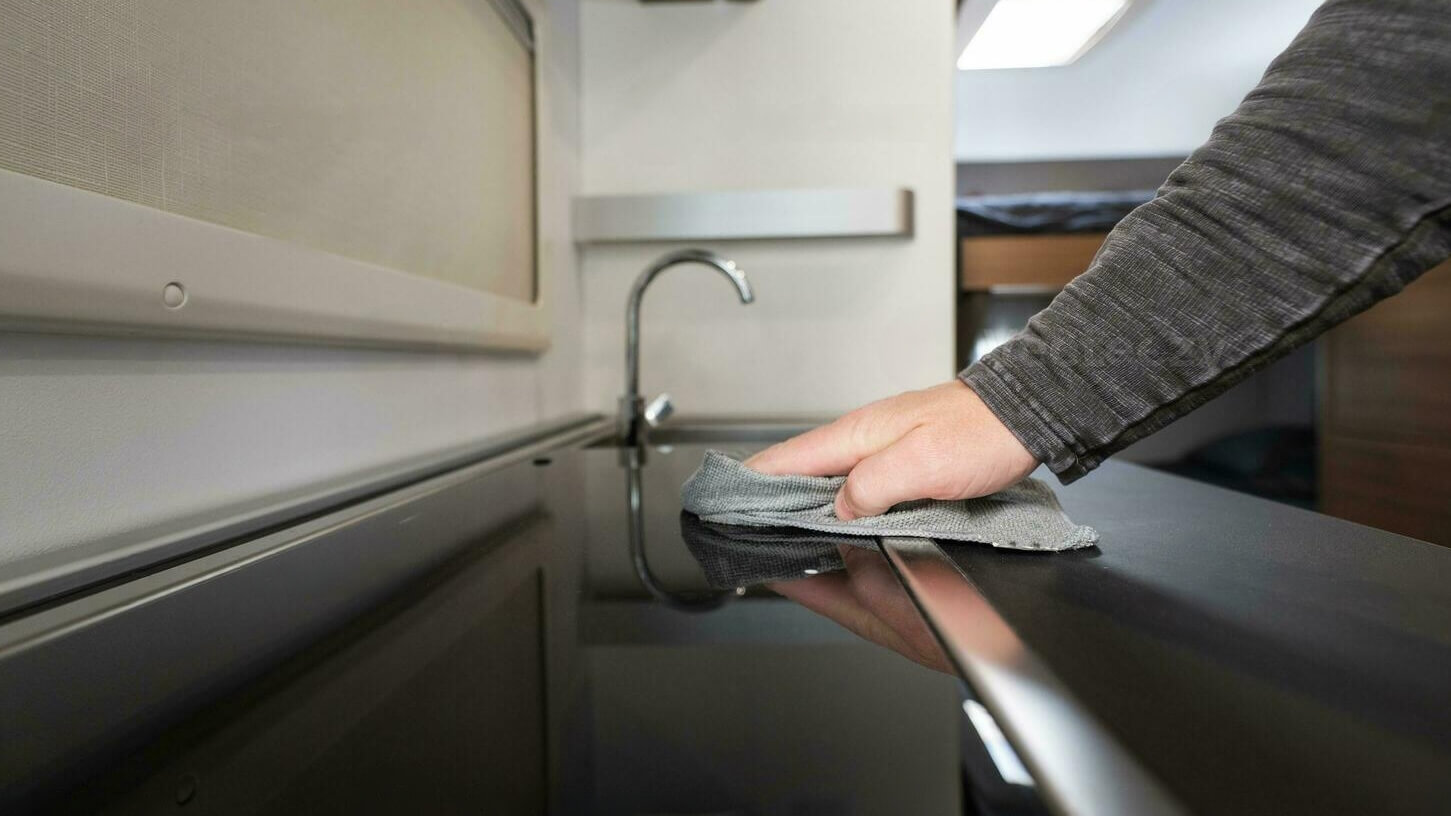 Persona limpiando la cocina de una autocaravana con un paño de microfibra