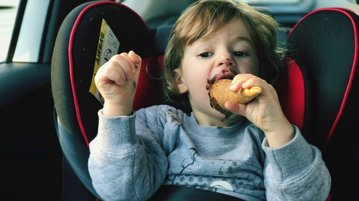 Bebé con la boca manchada de chocolate en la sillita del coche comiendo un dulce