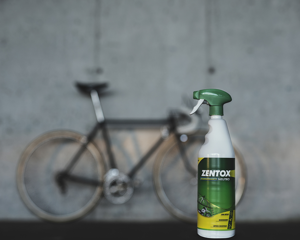 Botella de Zentox Desengrasante Neutro con una bicicleta de fondo apoyada en un muro de hormigón gris