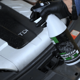 Persona con guantes negros pulverizando MotorClean sobre el motor de un coche