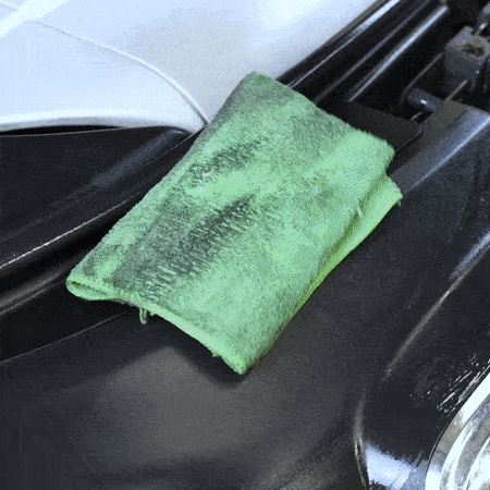 Persona con guantes negros limpiando un motor con una microfibra verde llena de grasa