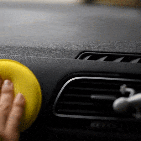 Una mano de una persona aplicando Sisbrill Car con un aplicador de poliespuma amarillo en un salpicadero de un coche