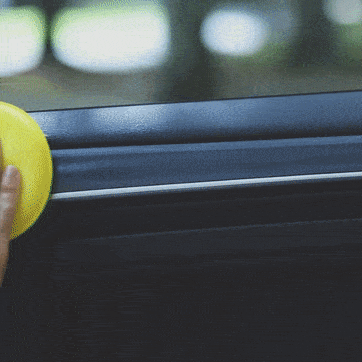 Una mano de una persona aplicando Sisbrill Car con un aplicador de poliespuma amarillo sobre los plásticos de la puerta de un coche
