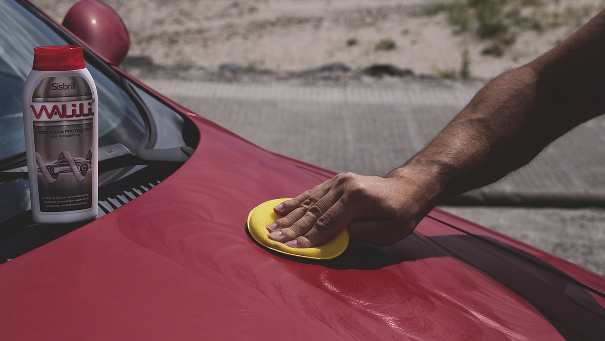 Hombre aplicando Walili Cera de Carnauba en un capó de un coche rojo con un aplicador de poliespuma amarillo