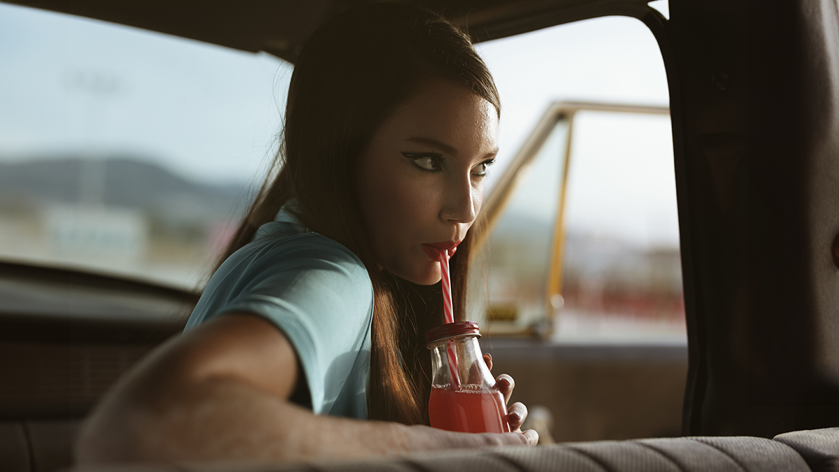 Mujer en el interior del coche bebiendo un refresco de cola con una pajita