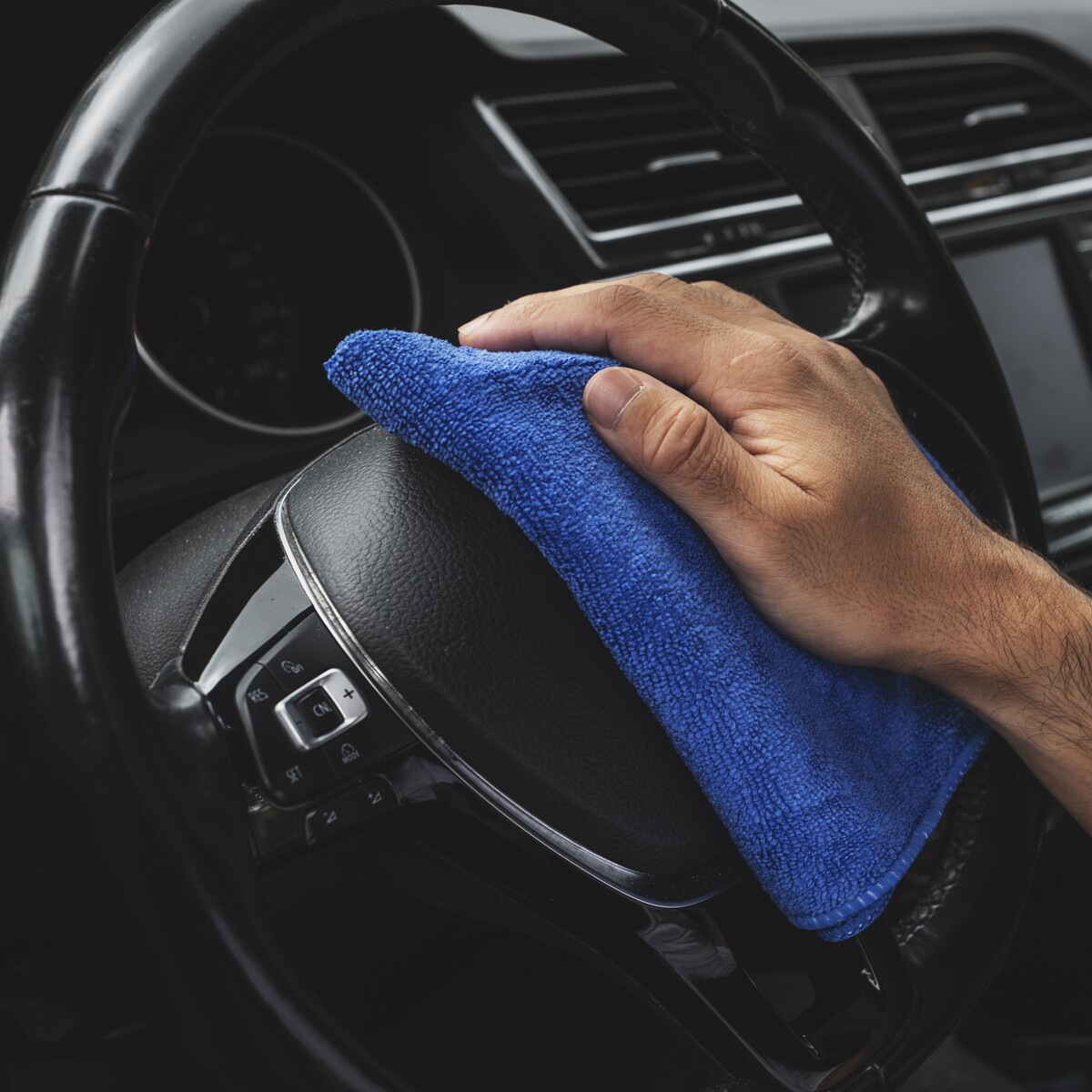 Hombre limpiando el volante de un coche con una microfibra azul