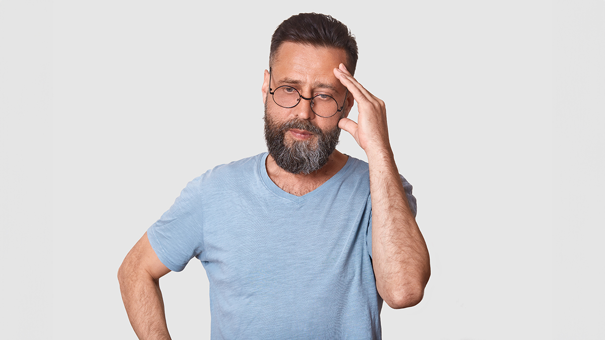 Un hombre con barba y gafas se agarra la cabeza con expresión pensativa.