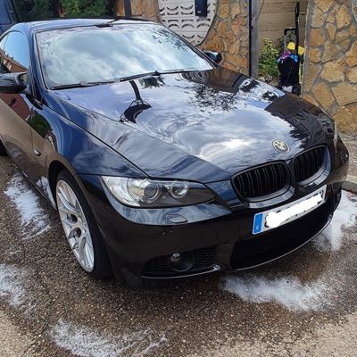 Coche BMW negro recién lavado, con espuma de champú aún visible en el suelo alrededor del vehículo, reflejando su brillo.