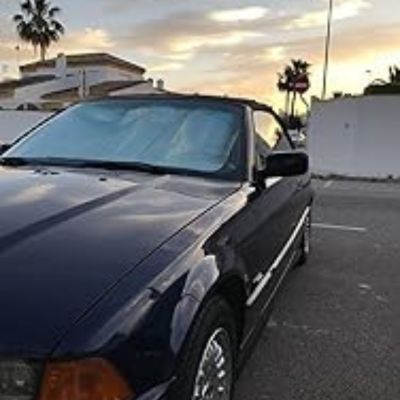 Coche descapotable negro con la pintura billante estacionado al aire libre al atardecer, con casas y palmeras visibles al fondo.