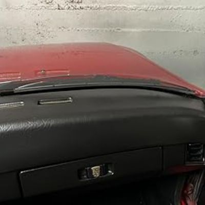 Salpicadero de un coche clásico, probablemente un Porsche, con un acabado en cuero negro y parte del capó rojo visible desde el interior.